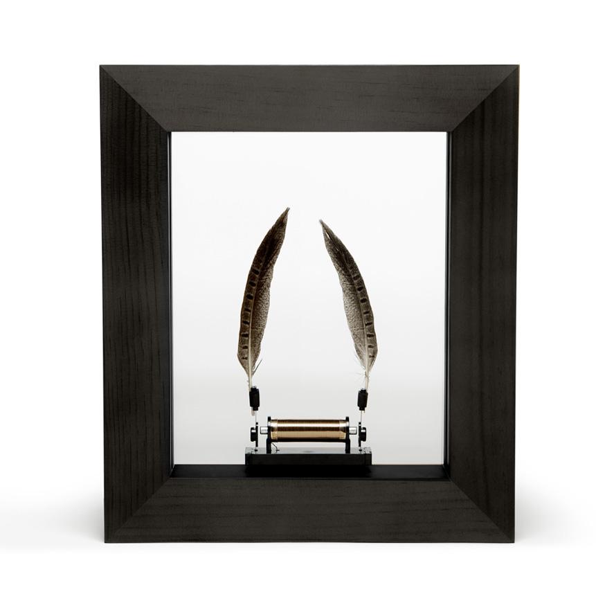 Framed kinetic sculpture with two feathers powered by a mechanism.